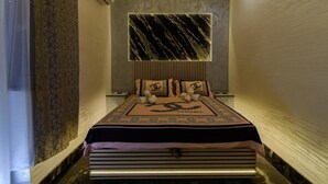 Une chambre moderne avec un lit placé au centre, sous un mur décoré d’un motif marbré, un lustre et une couvre-lit ornée d’un logo.