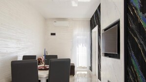 Una zona de menjador moderna amb taula blanca, cadires negres i un televisor gran penjat a la paret.