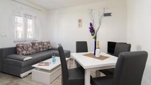 Un salon moderne avec un canapé gris, une table basse blanche et une table à manger avec des chaises. On peut voir un vase décoratif avec des fleurs violettes sur la table à manger.