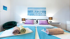 A hotel room with two beds, a green chair, a painting of sailboats, and a white dresser. - Apartment in Split with Balcony, Air condition, WIFI (5141-1) (Split)