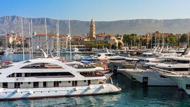 A marina with multiple yachts docked, a prominent building with a tower in the background, and a mountainous landscape. - Apartment in Split with Balcony, Air condition, WIFI (5141-1) (Split)