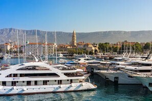 A marina with multiple yachts docked, a prominent building with a tower in the background, and a mountainous landscape. - Apartment in Split with Balcony, Air condition, WIFI (5141-1) (Split)