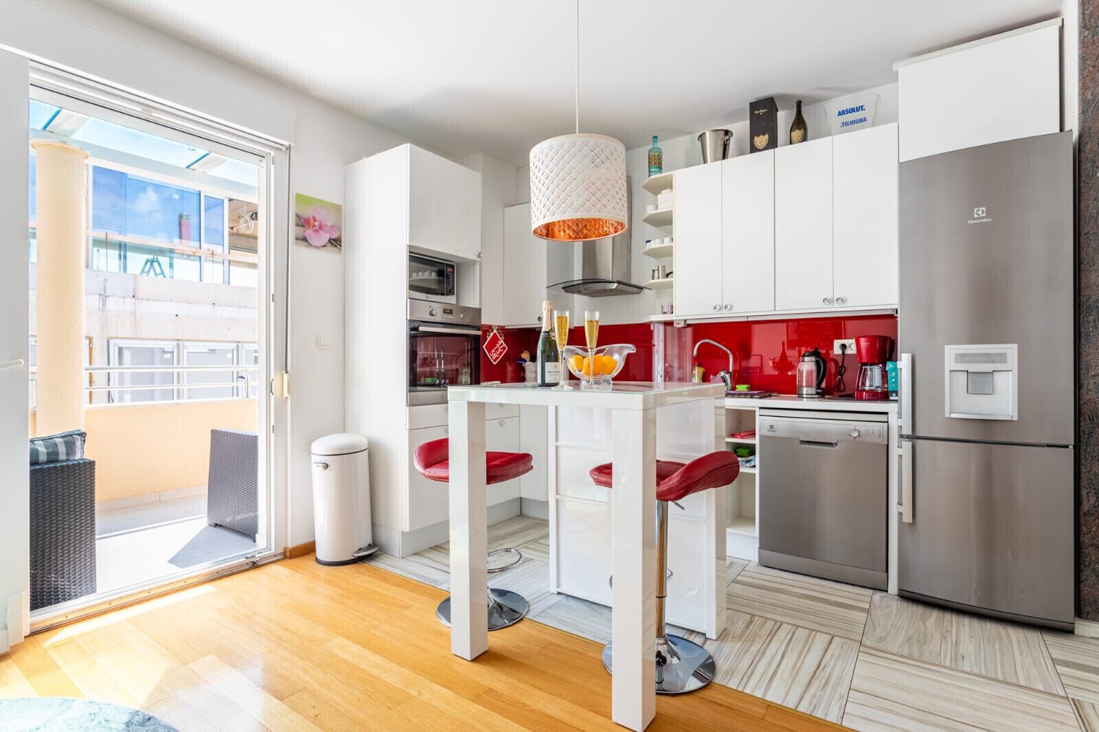 Eine moderne Küche mit weißen Schränken, einem Edelstahlkühlschrank und einem Essbereich mit weißem Tisch und roten Stühlen.