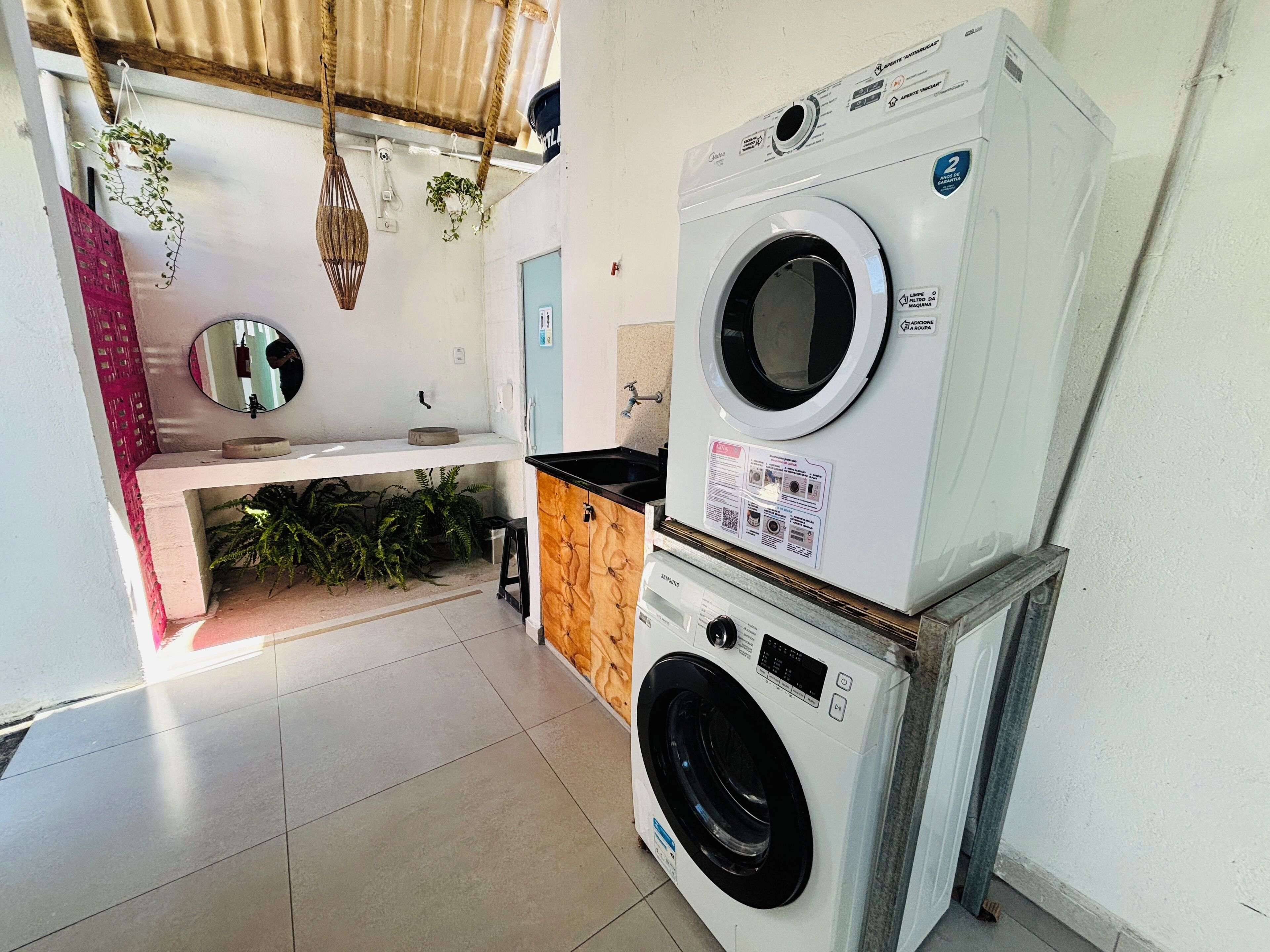 A laundry area with stacked washing machines, a sink, and hanging plants.