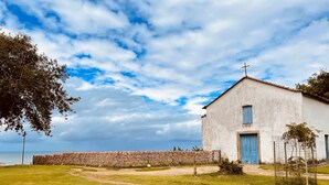 A white building with a blue door and a cross on top, surrounded by a grassy area and a stone wall. - Pousada Atenas (Porto Seguro)
