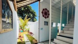 A modern interior with a staircase leading to a second floor, a small garden area with a pathway, and a security camera on the wall. - Pousada Atenas (Porto Seguro)