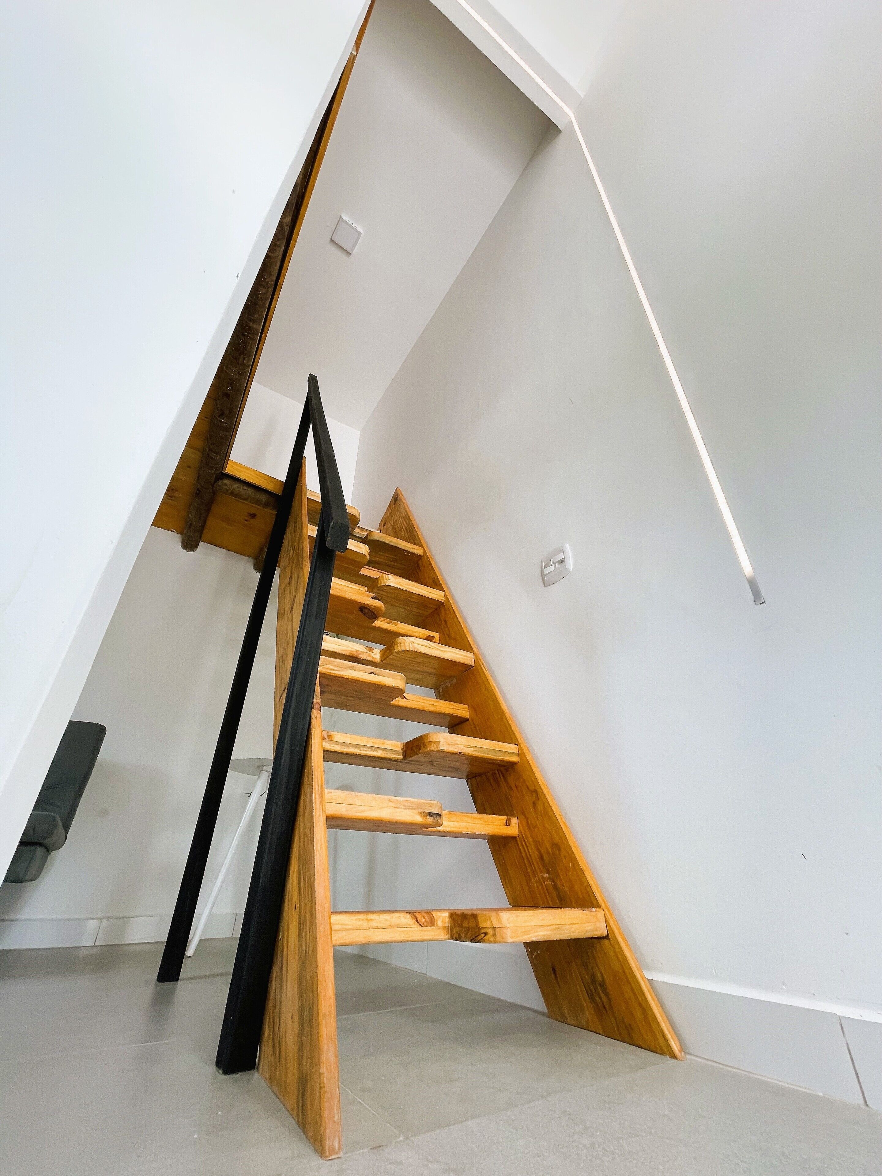Una escalera de madera en una habitación con paredes blancas y techo inclinado.