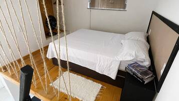 A bedroom with a bed, a hanging chair, a small rug, and a bedside table with books.