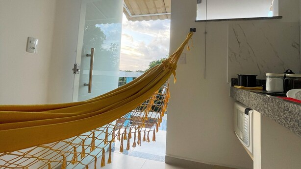 A modern kitchen with a hammock in the doorway, a view of the sky, and a sign that reads "Sonhos se realizam aqui!" - Pousada Atenas (Porto Seguro)