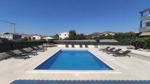 A rectangular swimming pool with a clear blue water surface, surrounded by a tiled deck. There are multiple lounge chairs aligned on both sides of the pool. - Apartment in Seget Vranjica with Seaview, Balcony, Air condition, WIFI (5142-3) (Seget Vranjica)