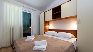 A hotel room with a bed, a wooden headboard, a built-in shelf, and a sliding door to a balcony. - Apartment in Seget Vranjica with Seaview, Balcony, Air condition, WIFI (5142-3) (Seget Vranjica)
