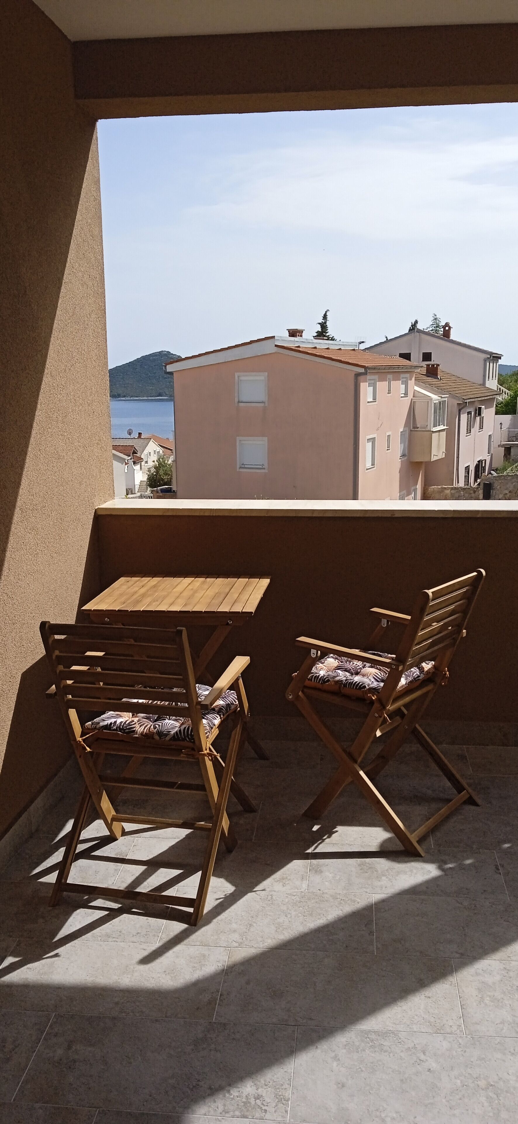 Un balcone con un tavolo di legno e due sedie, con vista su un corpo d'acqua e degli edifici.