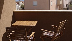 Ein Balkon mit Holztisch und zwei Stühlen, mit Blick auf ein Gewässer und Gebäude.
