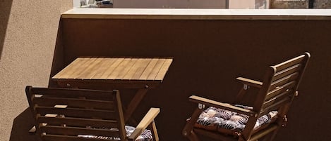 A balcony with a wooden table and two chairs, overlooking a body of water and buildings.