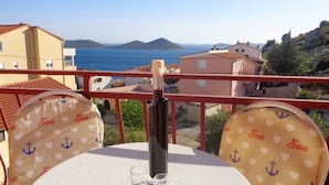 A table with a bottle and glasses, overlooking a coastal view with houses and mountains.