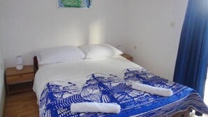 A neatly made bed with white and blue bedding, a small bedside table with a lamp, and a wall-mounted picture.