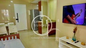Una habitación de hotel moderna con cama, televisor, refrigerador, mesa de comedor y sillas.