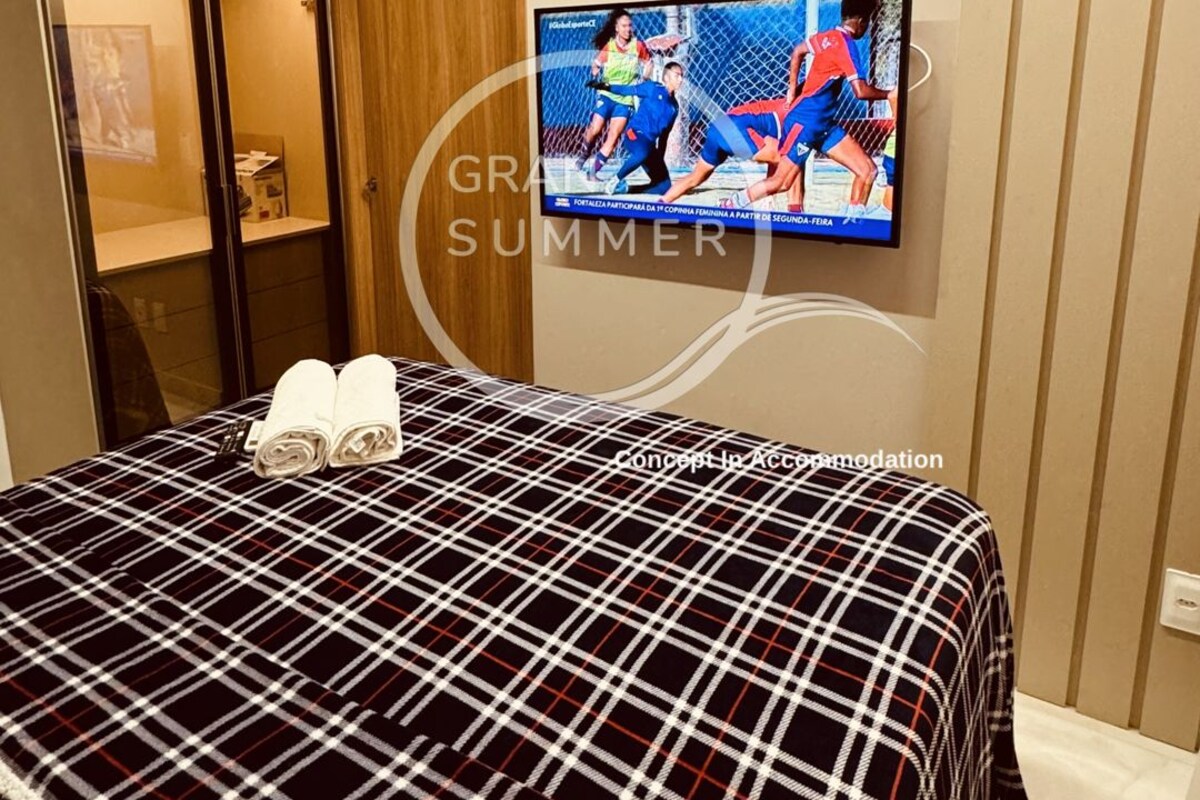 A hotel room with a bed, a television mounted on the wall, and a wooden wardrobe.