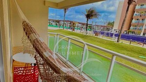 Un balcón con una hamaca, una silla roja y vistas a un césped verde y edificios.