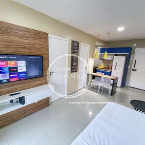 A modern hotel room with a flat-screen TV, a wooden accent wall, a kitchen area with a refrigerator, and a dining table with chairs. - Gran Summer Concept In Accommodation (Fortaleza)