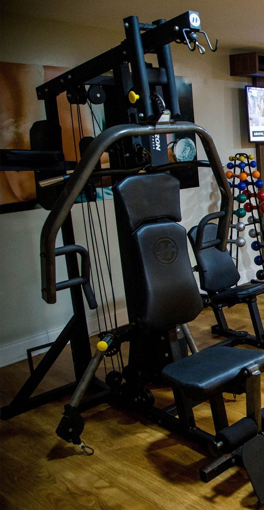 A gym with a variety of exercise equipment including a bench press, a squat rack, and a cable machine.