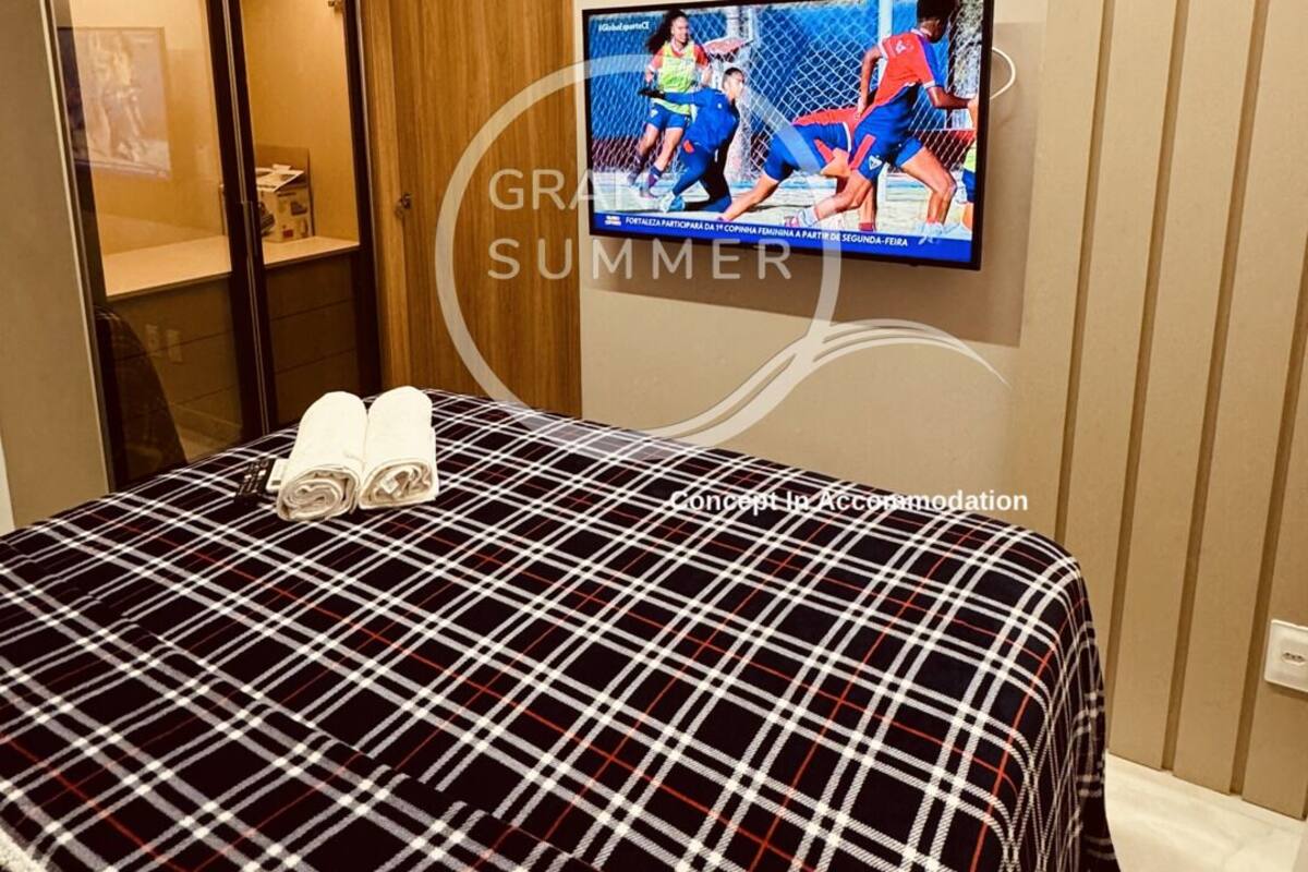 Ett hotellrum med en säng, en tv som är monterad på väggen och en garderob i trä.