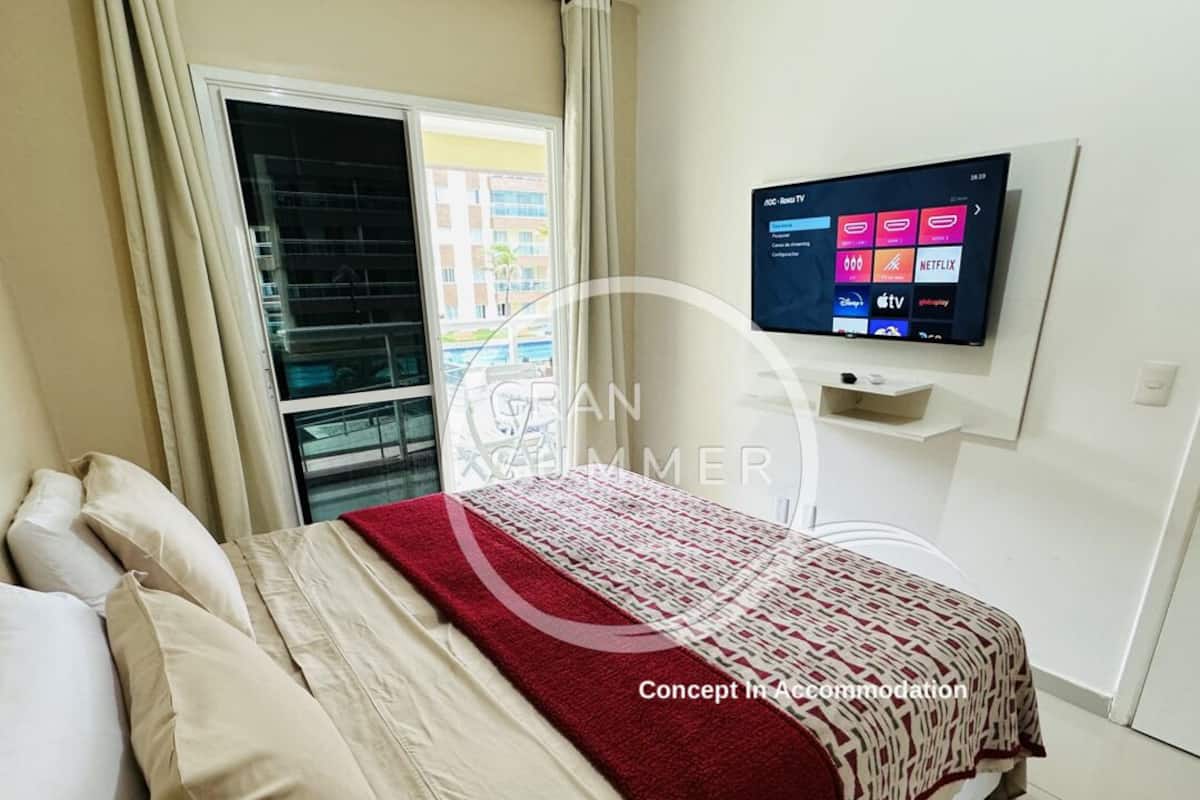 Ett hotellrum med en säng, en tv som är monterad på väggen och ett fönster med gardiner.