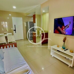 Una habitación de hotel moderna con cama, televisor, refrigerador, mesa de comedor y sillas.