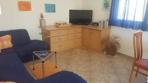 Ein Wohnzimmer mit einer Couch, einem Fernseher, einem Holzschrank und einer Topfpflanze.