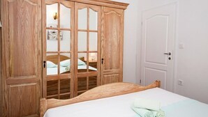 A bedroom with a wooden wardrobe, a bed with a white mattress, and a white door. - Apartment in Duće with Terrace, Air condition, WIFI, Dishwasher (5146-8) (Duce)