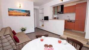 A modern living room with a round dining table, a sofa, and a kitchen area with red cabinets. - Apartment in Duće with Terrace, Air condition, WIFI, Dishwasher (5146-8) (Duce)