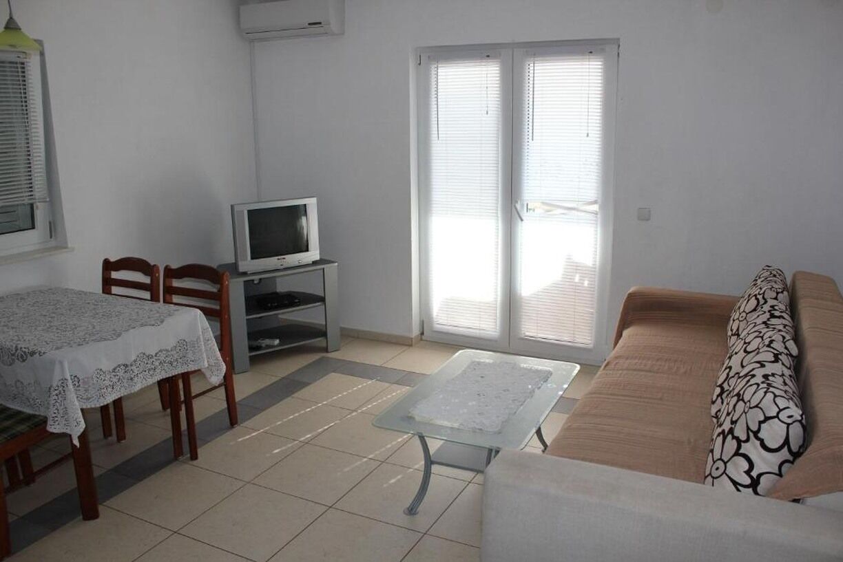 Een woonkamer met een bank, een salontafel, een televisie en een eethoek met stoelen en een tafel.