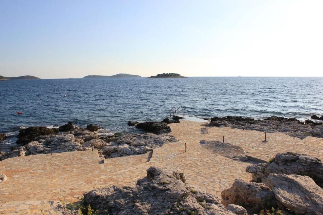 Ein Küstenwanderweg mit Steinpflasterung, felsigem Gelände und Blick auf das Meer und entfernte Inseln.