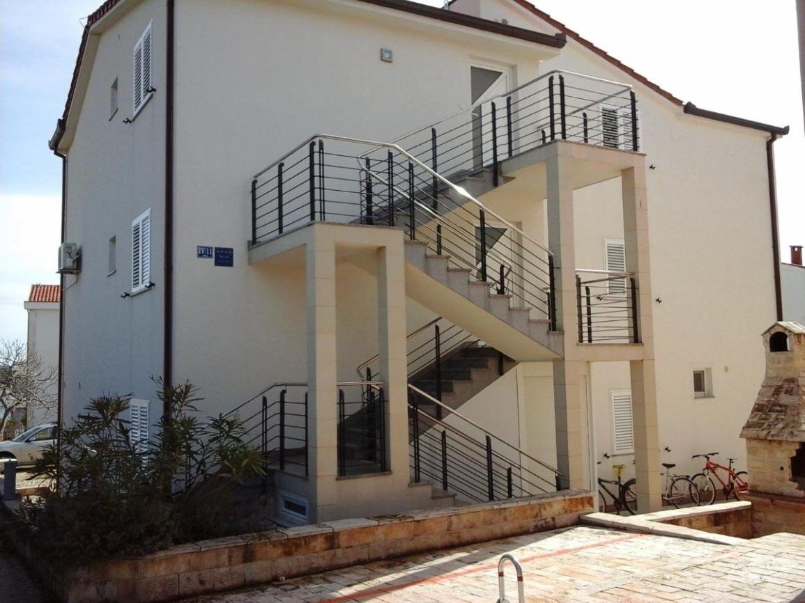 A two-story building with a central staircase, balconies, and a small garden area.
