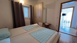 Ein Schlafzimmer mit zwei Betten, einem Kleiderschrank, einem kleinen Tisch und Blick auf einen Balkon.