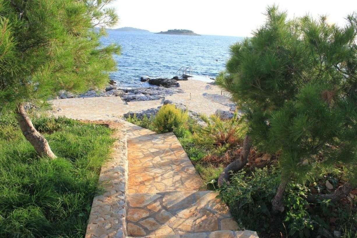 A stone pathway leading to a rocky beach with pine trees.