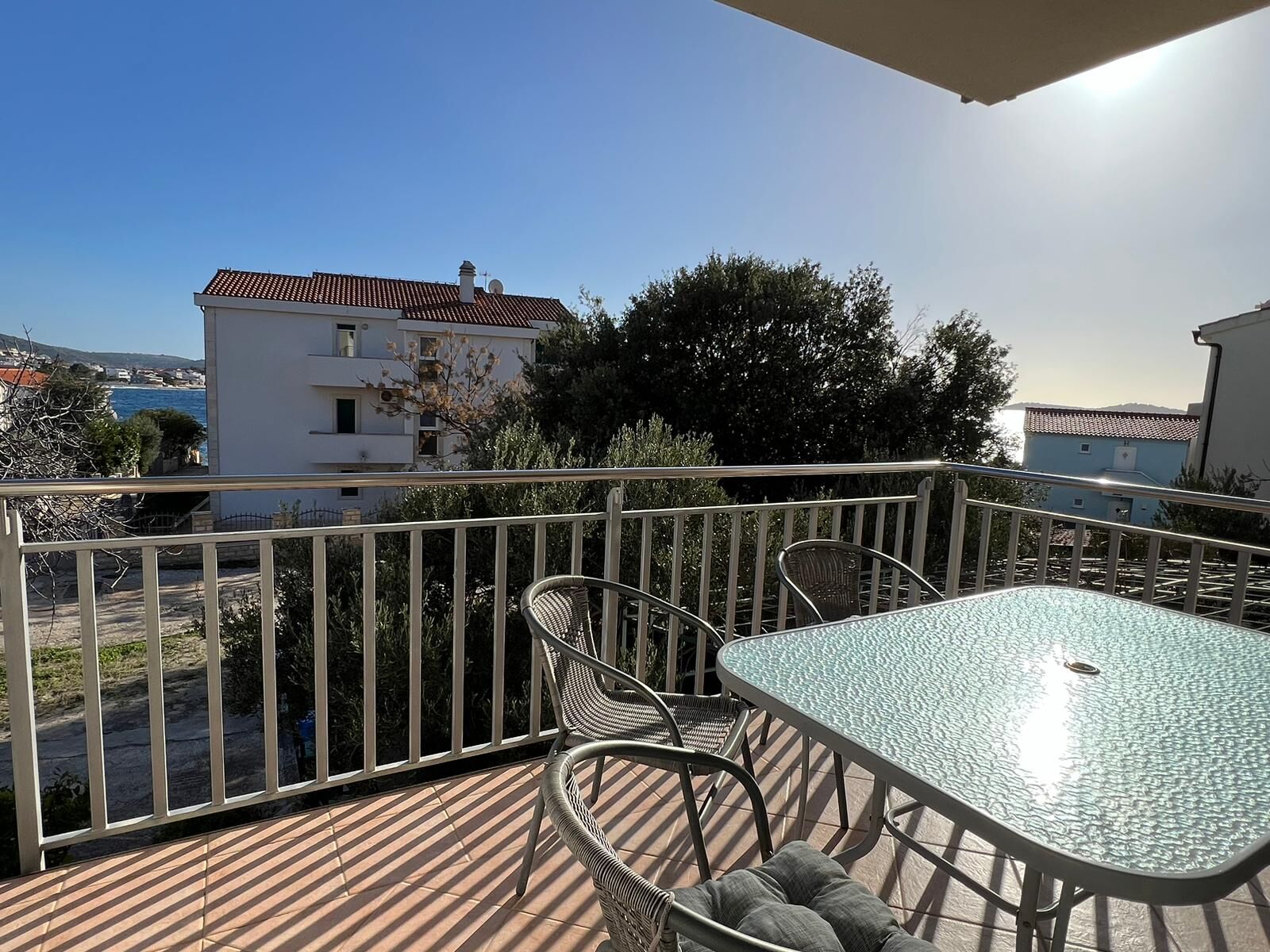 A balcony with a table and chairs, overlooking a coastal area with buildings and trees.