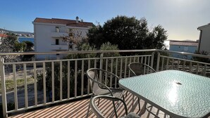 Ein Balkon mit Tisch und Stühlen mit Blick auf eine Küstenlandschaft mit Gebäuden und Bäumen.