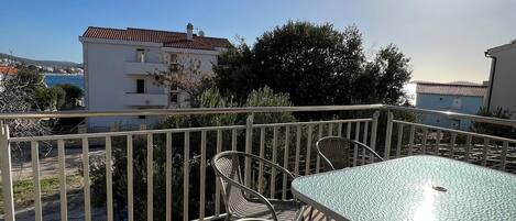 A balcony with a table and chairs, overlooking a coastal area with buildings and trees.