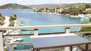 Ein Balkon mit Tisch und Stühlen mit Blick auf einen Yachthafen, einen Strand und einen Hügel mit Häusern.