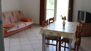 A dining area with a table and chairs, a sofa with a striped cushion, and a television on a stand. - Apartment in Ražanj with Seaview, Balcony, Air condition, WIFI (5150-4) (Ražanj)