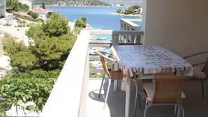 A balcony with a table and chairs, overlooking a coastal area with a clear view of the sea and distant hills. - Apartment in Ražanj with Seaview, Balcony, Air condition, WIFI (5150-4) (Ražanj)