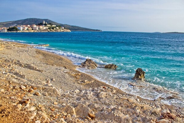 A rocky beach with clear turquoise waters and a distant village. - Apartment in Primošten with Seaview, Terrace, Air condition, WIFI (5155-1) (Primošten)