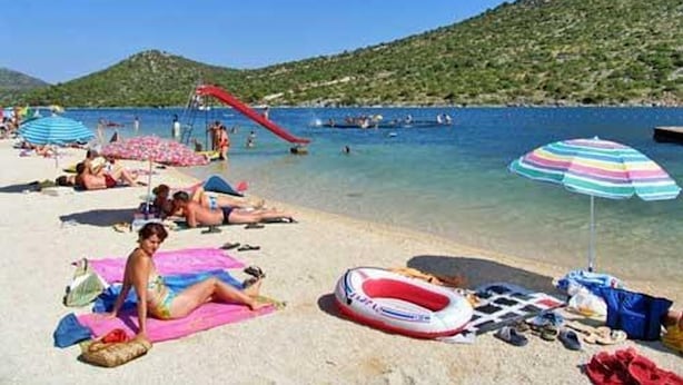 A beach with people sunbathing, a red slide, and clear blue water. - Apartment in Stupin Čeline with Seaview, Balcony, Air condition, WIFI (5149-1) (Podglavica)