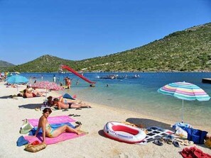 Ein Strand mit badenden Menschen, einer roten Rutsche und klarem, blauem Wasser.