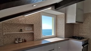 A modern kitchen with a view of the sea, featuring a large window, a gas stove, and a tiled backsplash.