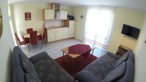 A living room with a sofa set, a dining table, and a kitchen area with cabinets and a TV. - Apartment in Rogoznica with Seaview, Balcony, Air condition, WIFI (5153-2) (Rogoznica)