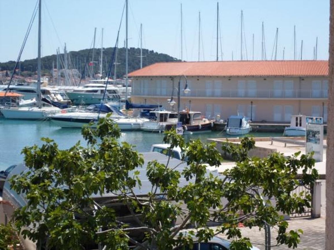 A marina with boats docked, a building with a red roof, and a hill in the background.