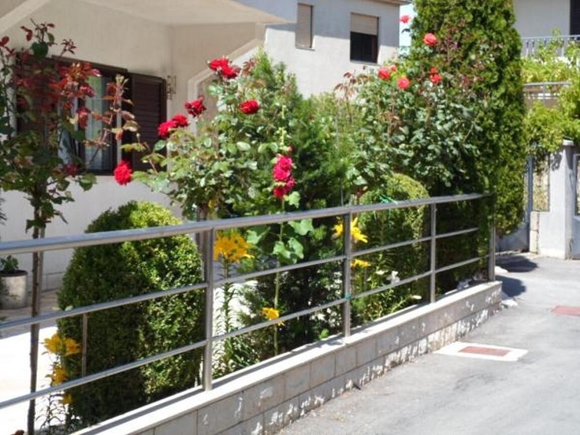 Un balcon doté d’une rambarde en métal, entouré d’une végétation luxuriante et de fleurs rouges.