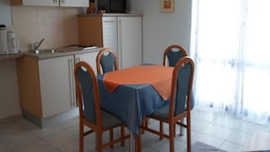 A compact kitchen with white cabinets, a microwave, and a coffee maker. There is a dining table with four chairs, and a window with curtains.
